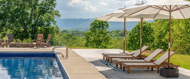 Resort pool deck with lounge chairs, umbrellas, and mountain valley views beyond landscaped grounds