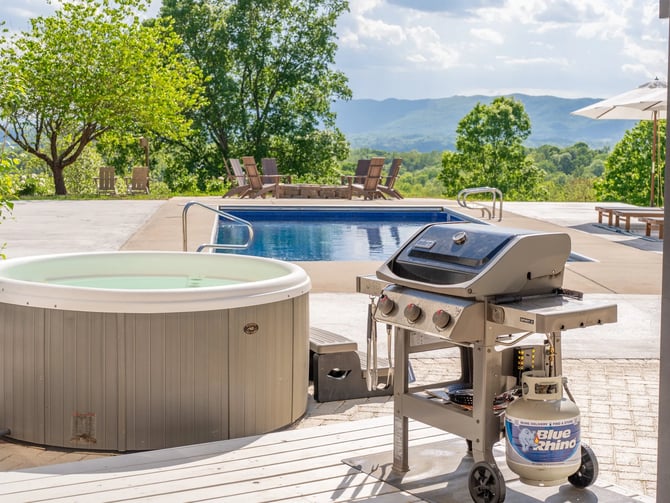 Hot tub and gas grill on patio overlooking swimming pool and mountain valley landscape