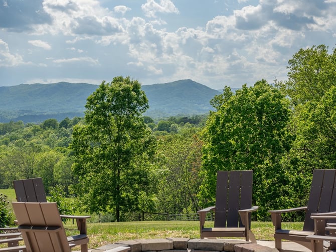 Patio with Adirondack chairs surrounding stone fire pit, mountain and forest view beyond
