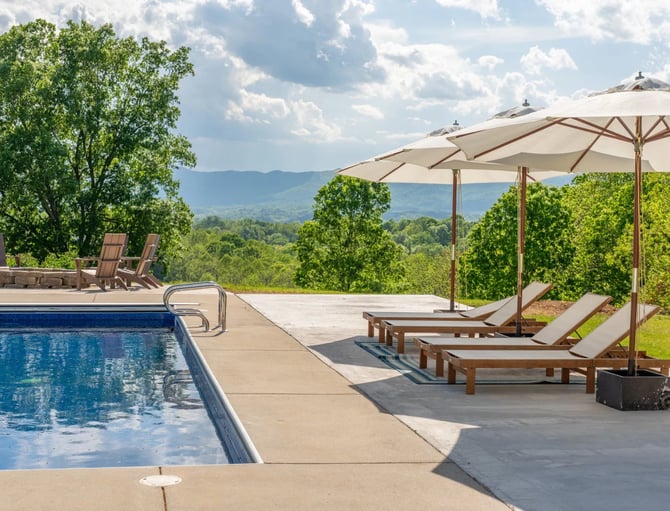 Swimming pool with lounge chairs and umbrellas overlooking forested valley and distant mountains